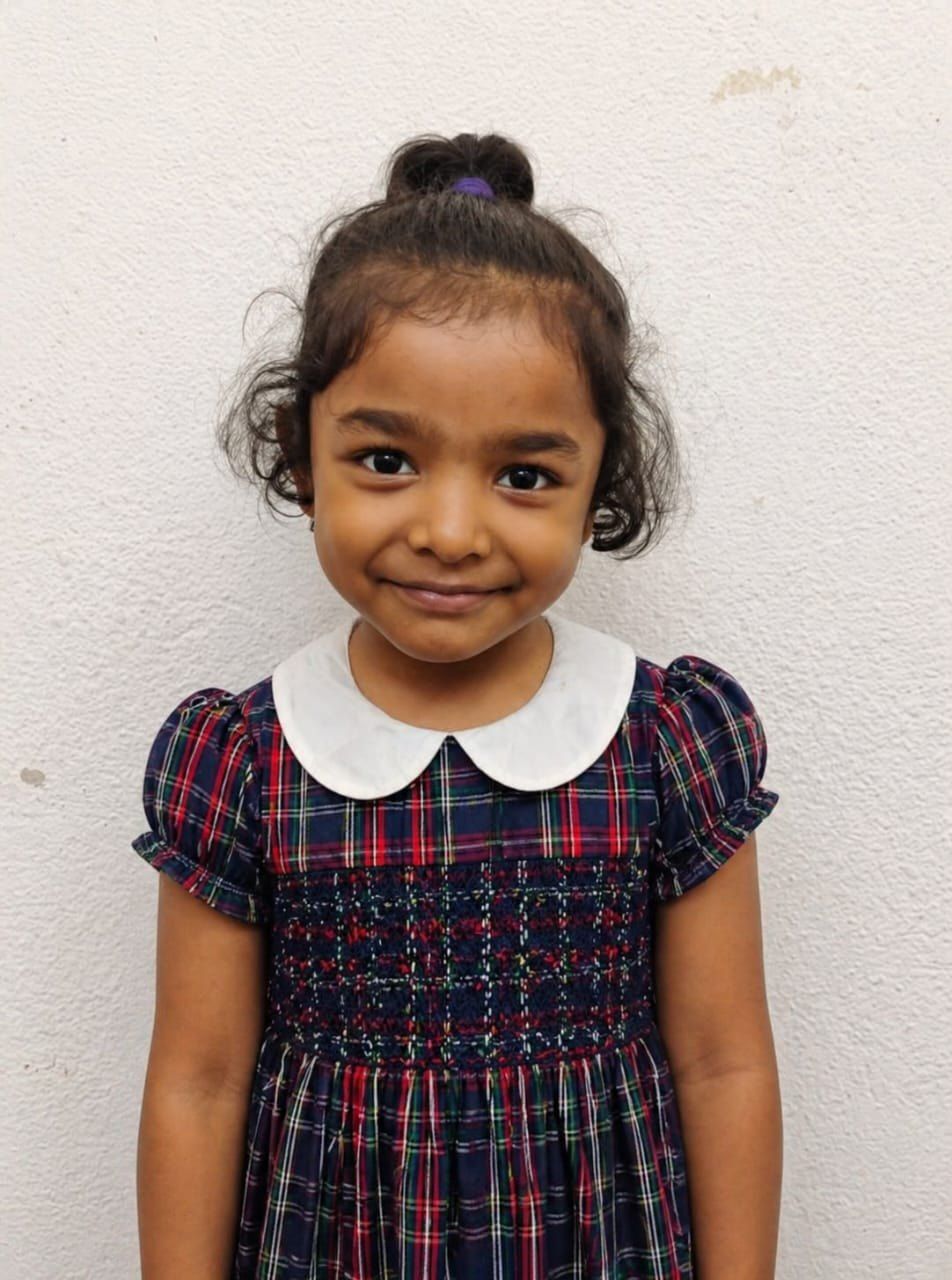 A smiling IGPS student in the checked smocked dress with a white collar